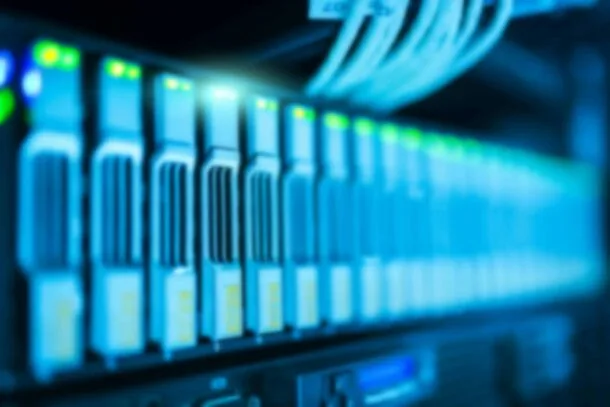 A row of blurred, illuminated server racks with network cables connected, indicating an active data center environment. {{brizy_dc_image_alt imageSrc=